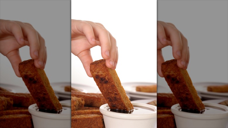 young child with hand dipping french toast in syrup
