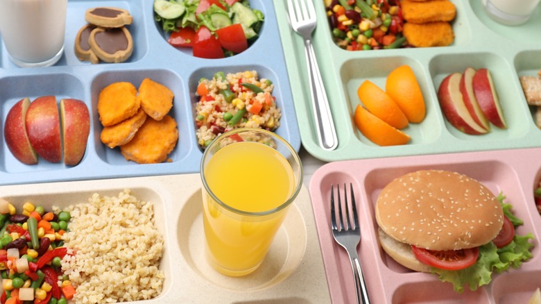 Plastic trays with tasty food, milk and orange juice on table, above view. School lunch