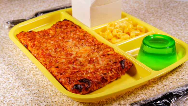 Old fashioned cafeteria school lunch tray with rectangle pizza with small carton of milk mac-n-cheese and green gelatin for dessert
