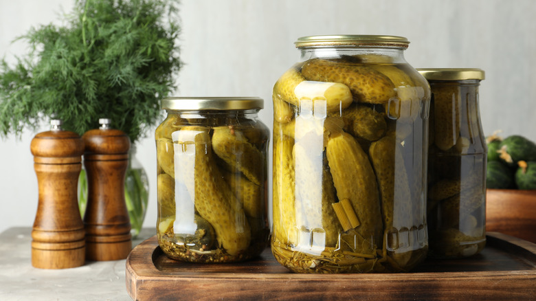 jar of pickles on wooden board with spice grinders and fresh herbs
