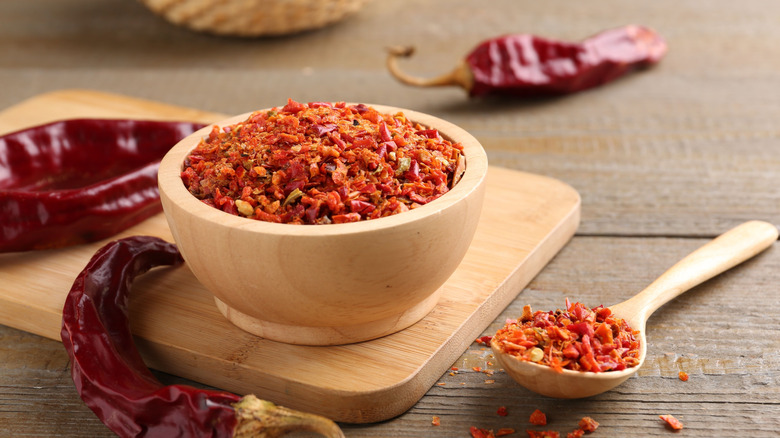 red pepper flakes in dish with spoon and dried red peppers
