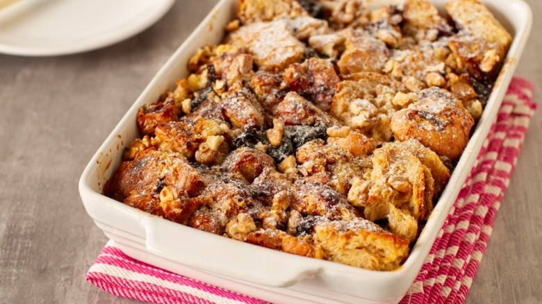 a casserole dish of bread pudding with powdered sugar sits on a red and white cloth