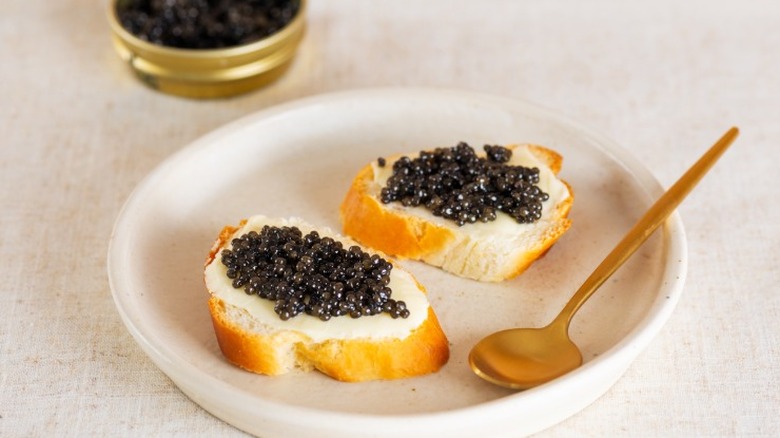 a white plate with two small bread rounds topped with caviar