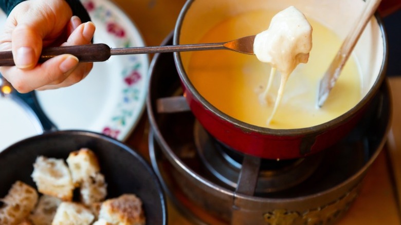 pieces of bread being dipped into a pot of fondue