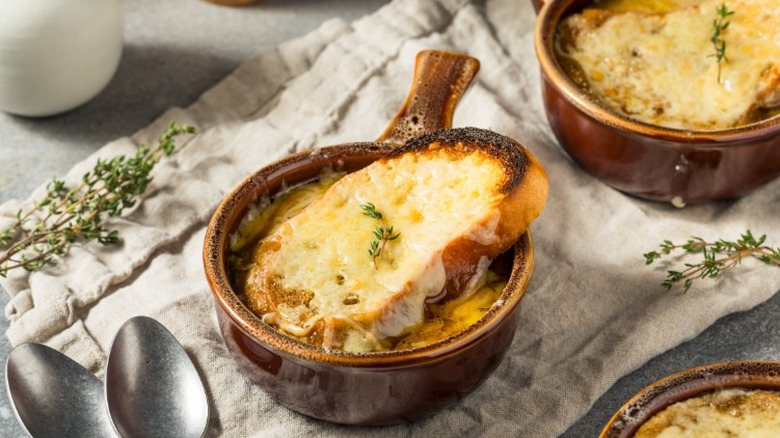 two bowls of french onion soup with slices of bread on a white cloth with spoons