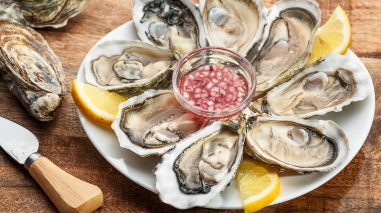 a plate of oysters with lemon slice and a small bowl of pink-colored sauce in the center