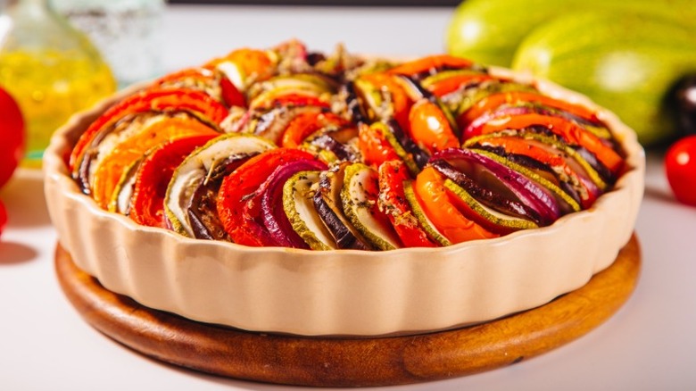 a round dish of ratatouille sits on a white counter with vegetables in the background