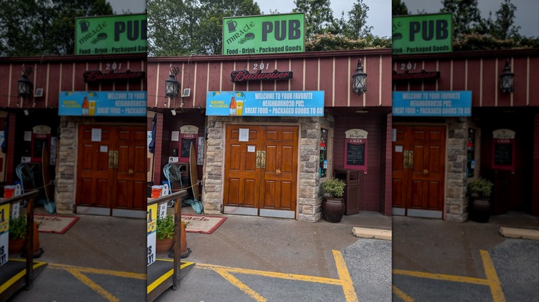 Exterior of Miracle Pub from parking lot with sign above wooden doorway