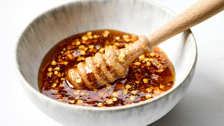 A bowl of hot honey with chili pepper flakes and honey dipper