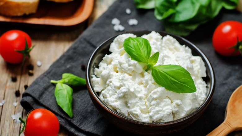 Ricotta cheese in bowl topped with fresh basil on folded cloth with basil leaves and cherry tomatoes