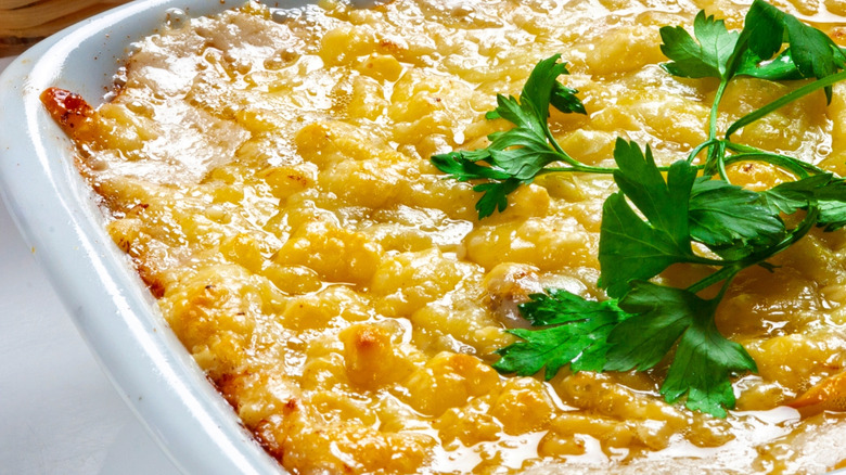 Upclose view of cheesy lasagna in a white baking dish topped with fresh parsley