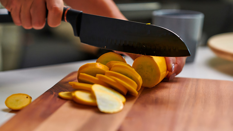 Close up of hand slicing yellow squash on cutting board in kitchen