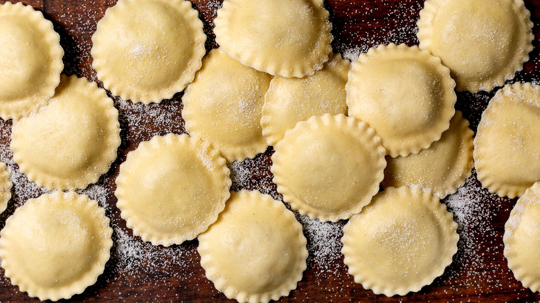 Homemade ravioli on a wooden surface sprinkled with flour