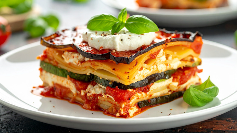 A piece of eggplant lasagna on a white plate topped with basil