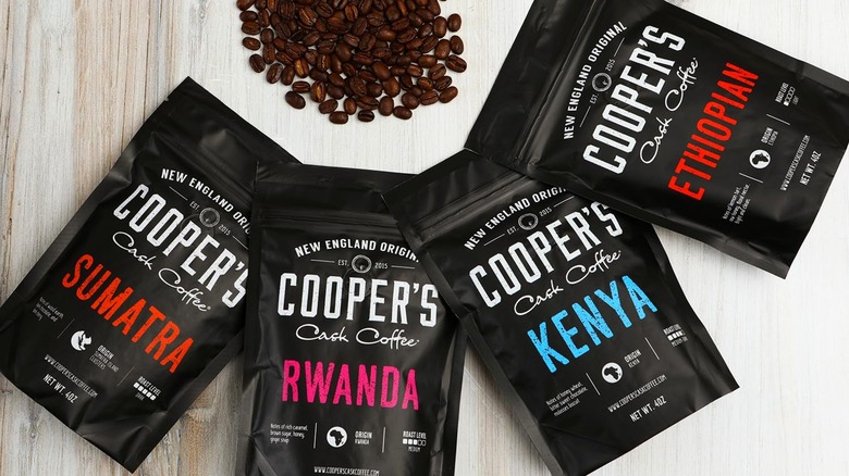 Four bags of different flavors of Cooper's Cask Coffee with a small pile of coffee beans.