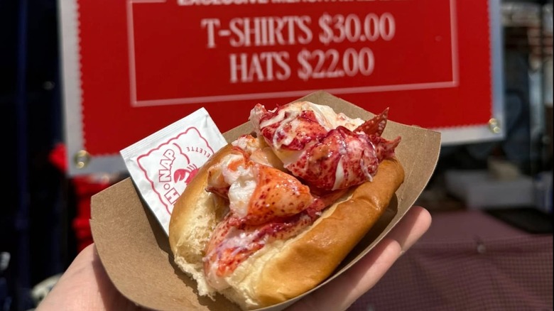 Hand holding a McLoons Lobster Shack lobster roll in a to-go carton with a wet napkin