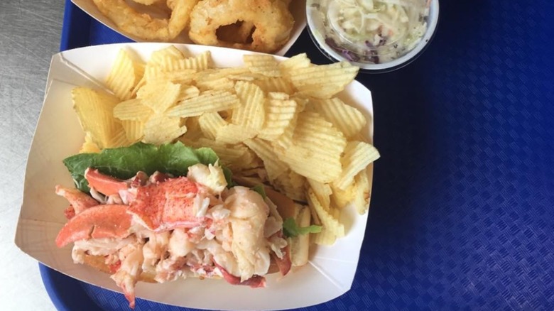 Five Islands Lobster Co. lobster roll in a to-go container with a side of chips, coleslaw, and onion rings