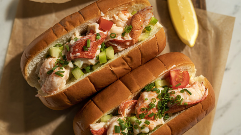 A two fresh lobster rolls on butcher paper with a lemon wedge
