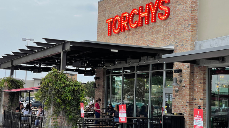 Exterior of a Torchy's Tacos restaurant, with customers sitting outside