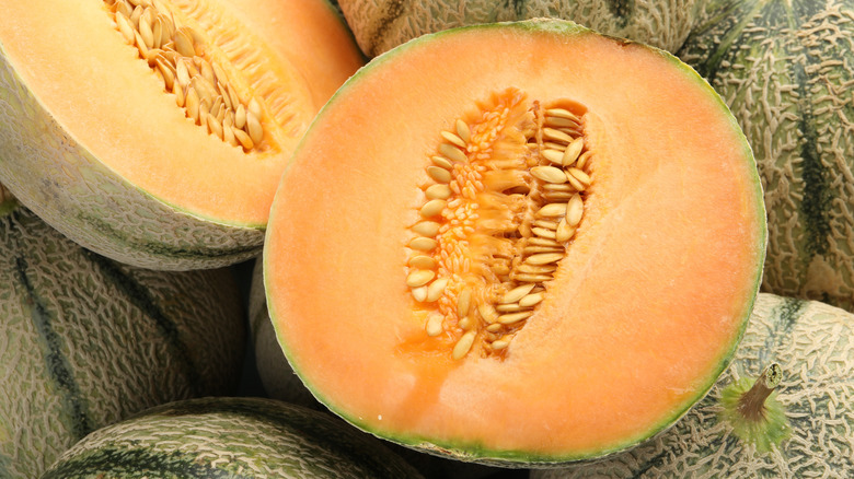 Bright orange cantaloupe cut open on pile of whole cantaloupes