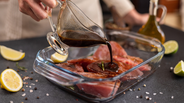 Person pouring marinade over fish in a glass dish