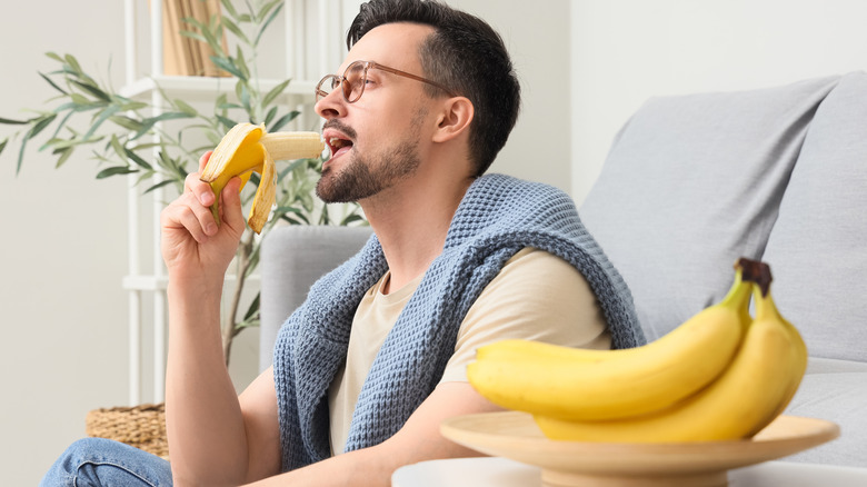 Man eating a banana next to a bowl of bananas