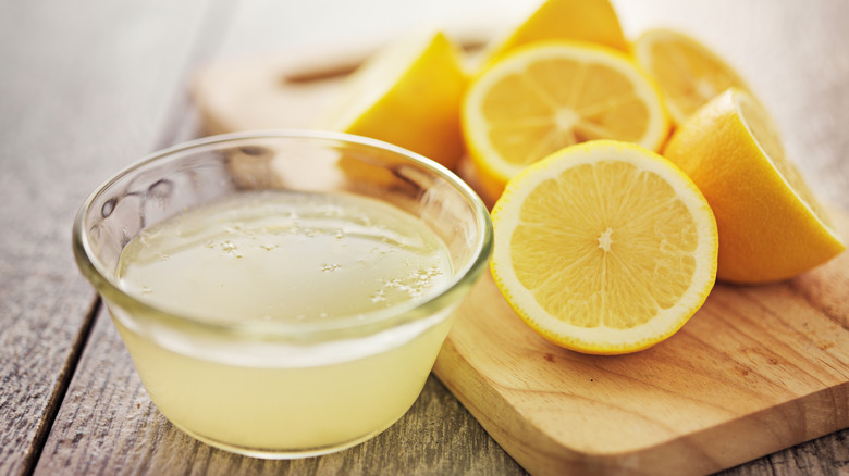 Lemon juice in a bowl next to cut lemons