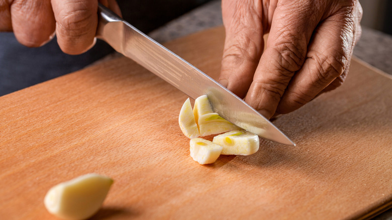 Hands slicing a garlic clove