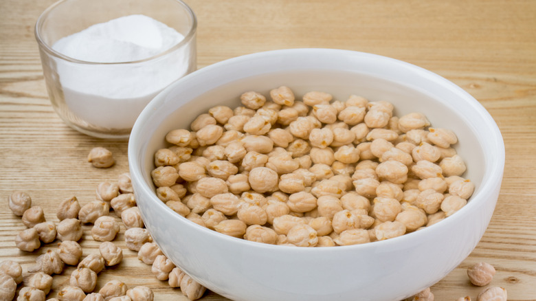 Chickpeas soaking in white bowl of water next to glass of baking soda