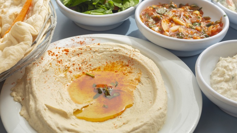 Creamy hummus on white plate topped with olive oil and spices, surrounded by side dishes