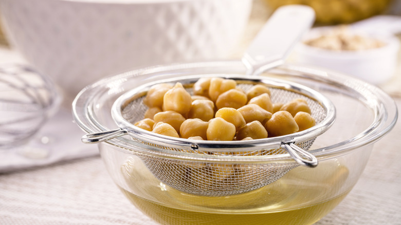 Cooked chickpeas in strainer over bowl of clear brown cooking liquid