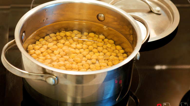 Chickpeas in metal pot of water on black stovetop