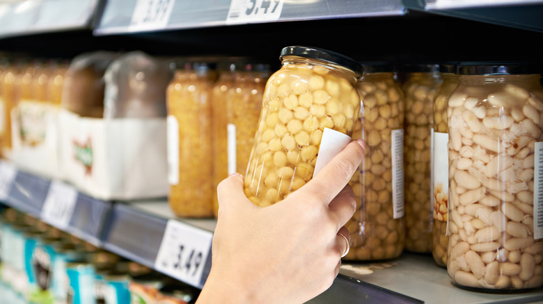 Hand grabbing jar of chickpeas off grocery store shelves