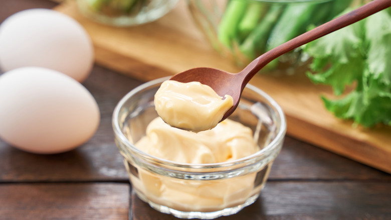 small bowl of mayo with brown spoon and whole eggs on the side