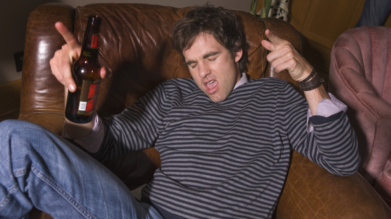 Man in a striped shirt sprawled in a recliner with a bottle of beer.