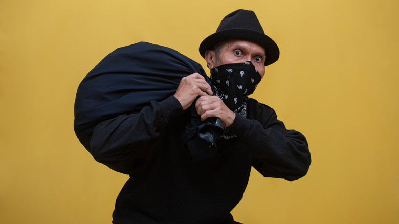 Thief in all black with a bandana covering their face carries a bag of loot.