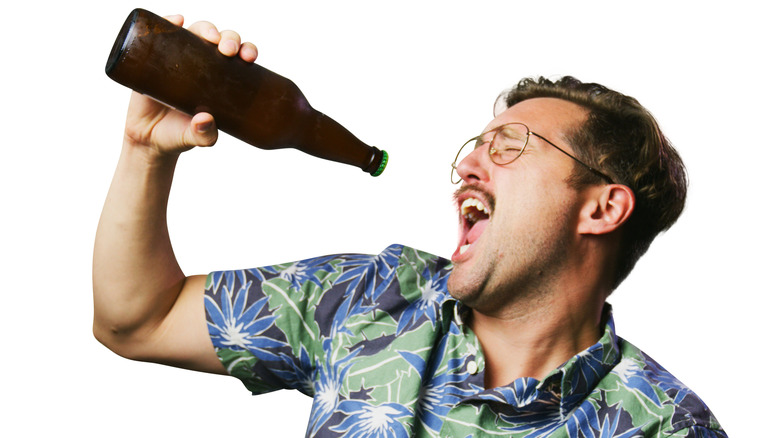 Man with moustache and Hawaiian shirt singing into a bottle of beer.