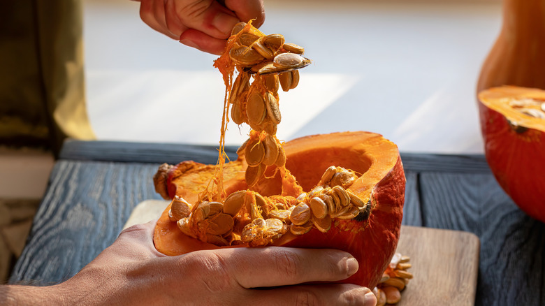 Hands cleaning a pumpkin and pulling out seeds