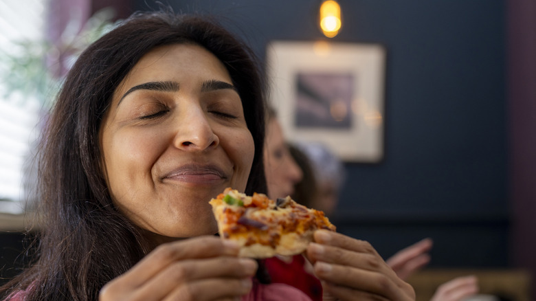 Smiling woman eating pizza with eyes closed