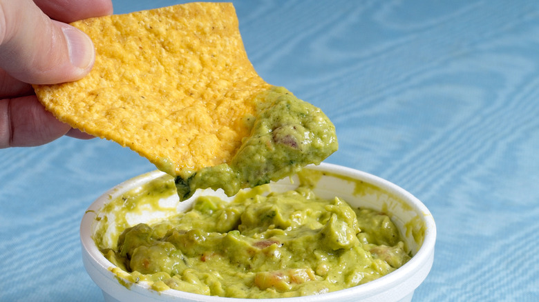 A person dipping chip in avocado dip