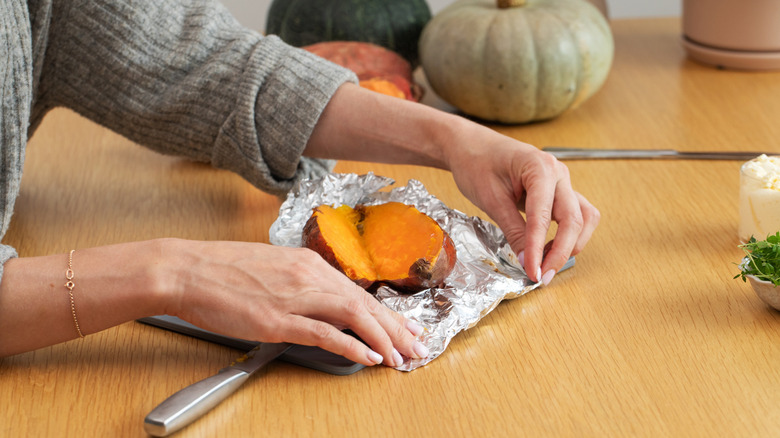 Female preparing sweet potato on cutting board with squash in background
