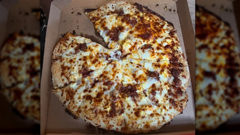 A Casey's bacon breakfast pizza in a box with a slice missing