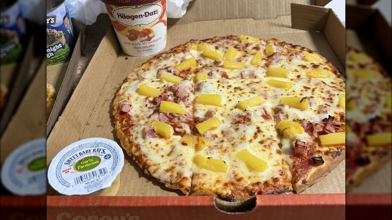 A Casey's Ultimate Hawaiian pizza in a box with a container of sauce and a container of Haagen-Dazs.