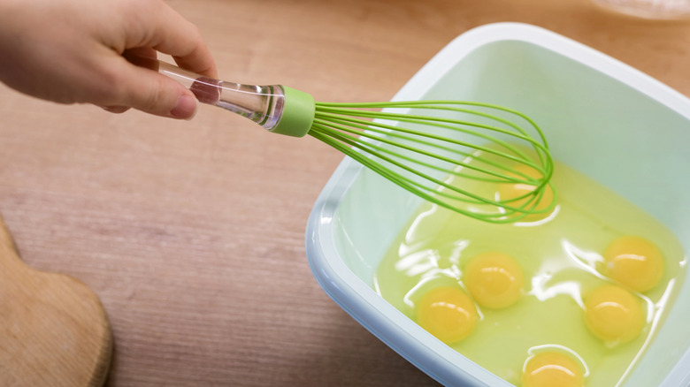Hand with green whisk over eggs in bowl