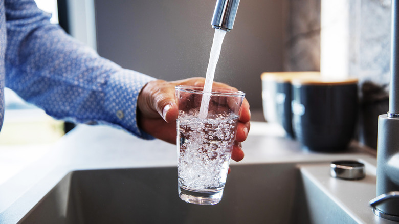 A male hand refilling a glass from a kitchen faucet.