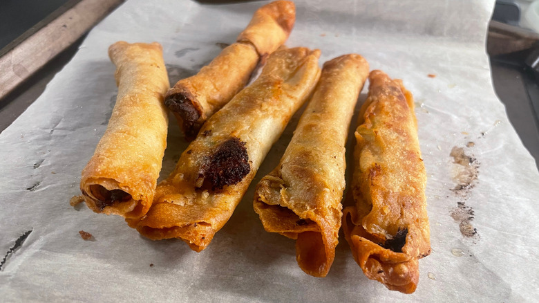 A bunch of frozen taquitos on an oven sheet.