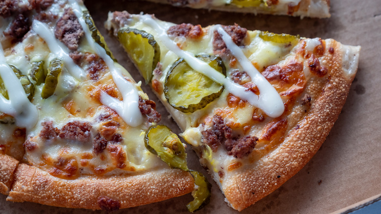 A close-up of a hamburger pizza with pickles