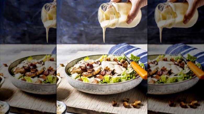 Hand pouring white salad dressing from jar onto salad