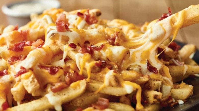Outback's Aussie cheese fries covered in cheese and bacon bits with one fry being picked up
