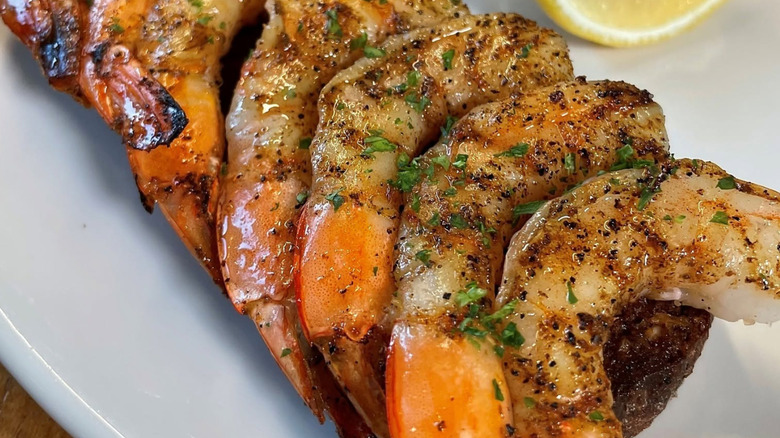 Up close of 6 grilled shrimp on a grilled piece of brown bread on a white plate